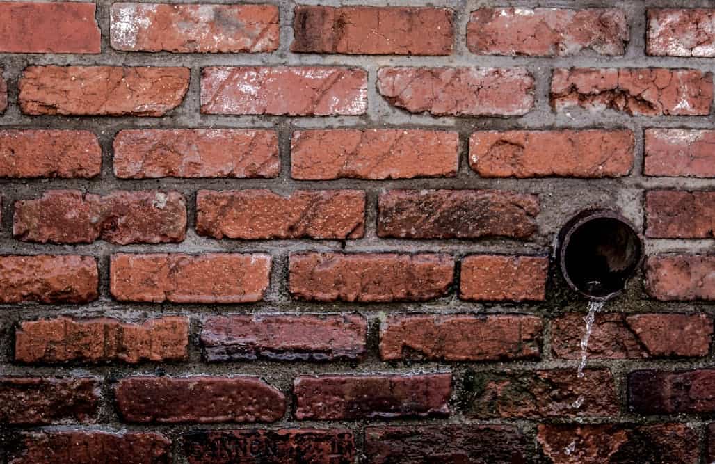 Pared de ladrillo con una tubería vertiendo agua residual